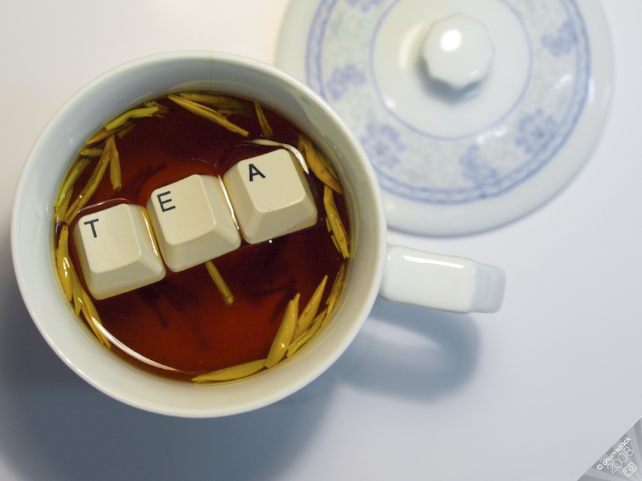 A photo of a white teacup on a white table. There is orange-red colored tea and small, folded yellow leaves in the teacup, as well as three floating white keyboard keys that spell out the word "TEA".